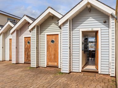A row of small wooden beach huts with one open door showing an interior kitchen and sea view at Beach Hut 5 in Shaldon