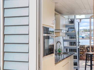 A kitchen area with a sink oven dishwasher and stairs leading outside to a patio with a view of water and boats at Beach Hut 5 in Shaldon