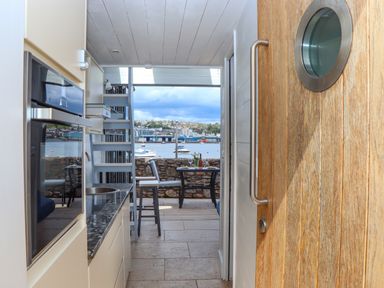 A small kitchen area with a countertop and sink next to a wooden door looking out to a dining table and chairs on a terrace overlooking water with boats at Beach Hut 5 in Shaldon