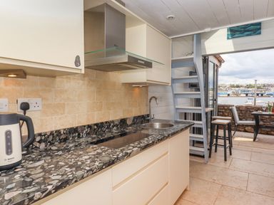A kitchen with a black patterned countertop and white cabinets next to a light blue staircase and open door leading to an outdoor seating area at Beach Hut 5 in Shaldon