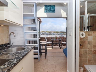 A kitchen with a sink and stove next to stairs leading to a balcony with a table and chairs overlooking water at Beach Hut 5 in Shaldon