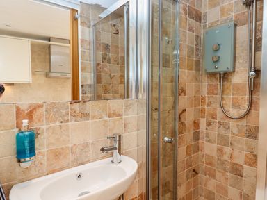 A bathroom with a sink soap dispenser and a shower with tiled walls at Beach Hut 5 in Shaldon