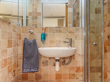 A small bathroom sink with a striped towel hanging beside it a soap dispenser above and a glass shower door to the right at Beach Hut 5 in Shaldon