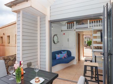 An outdoor dining area with a table and chairs next to a small interior space with a blue sofa and loft bed at Beach Hut 5 in Shaldon