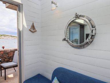 An interior corner with a blue sofa and a round nautical mirror on a white wooden wall at Beach Hut 5 in Shaldon