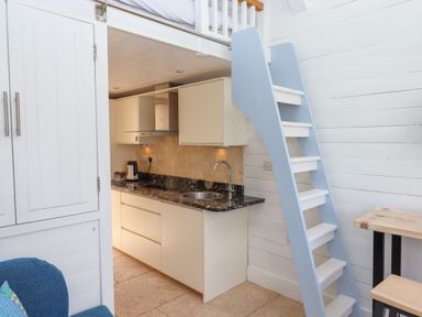 A small kitchen with black countertop white cabinets a blue and white ladder and a wooden table at Beach Hut 5 in Shaldon