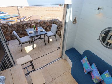 A small patio with a table and two chairs by a stone wall and a blue sofa with cushions inside at Beach Hut 5 in Shaldon