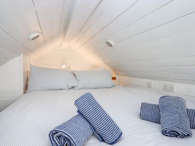 A bed with striped pillows and rolled striped towels in a white wooden loft bedroom at Beach Hut 5 in Shaldon