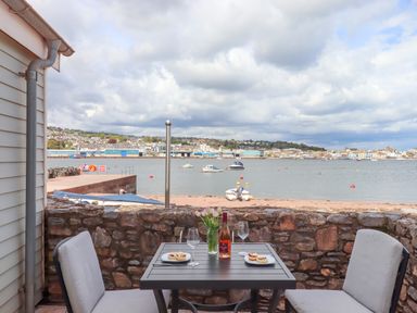 A patio table with two chairs overlooking a waterfront with boats and a town in the background at Beach Hut 5 in Shaldon