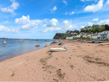 A sandy beach with boats on the shore and floating in the water near houses and a cliff at Beach Hut 5 in Shaldon