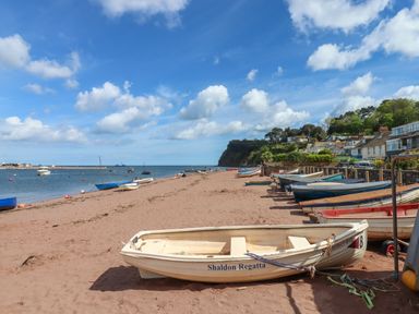 A sandy beach with boats lined up along the shore and houses on a hillside at Beach Hut 5 in Shaldon