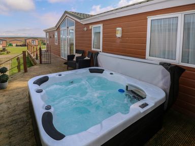 A hot tub on a wooden deck next to a brown cabin with windows and chairs at Gentle Tide L46 Hasguard Cross near Little Haven