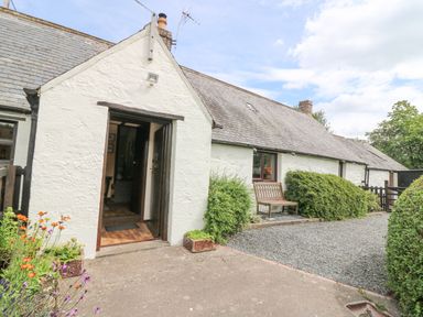 A white stone cottage with a wooden bench and gravel driveway at Loanview in Cornhill-On-Tweed