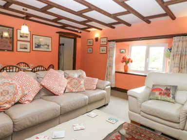 A living room with a beige sofa and armchair with patterned cushions a coffee table and framed pictures on orange walls at Loanview in Cornhill-On-Tweed