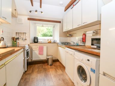 A kitchen with wooden countertops, white cabinets, washing machine, dishwasher, stove, and a window at Loanview in Cornhill-On-Tweed