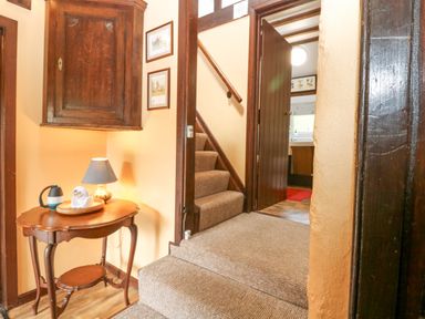 A stairway with carpet leading up from a small wooden table with a lamp and some items on it at Loanview in Cornhill-On-Tweed