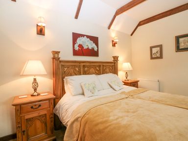 A bedroom with a large wooden bed with beige blankets and bedside tables with lamps at Loanview in Cornhill-On-Tweed
