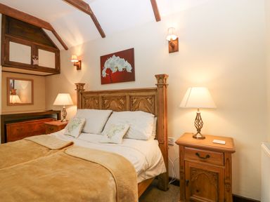 A bedroom with a wooden bed frame bedside tables lamps and a painting above the bed at Loanview Cornhill-On-Tweed