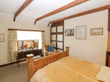 A bedroom with wooden bed frame dressing table with mirror armchair and framed pictures at Loanview Cornhill-On-Tweed