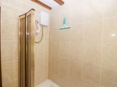 A shower area with beige tiled walls a white electric shower and a blue and white squeegee at Loanview Cornhill-On-Tweed