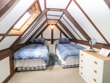 A bedroom with two single beds under a sloped ceiling with a small nightstand between them and a chest of drawers on the right at Loanview in Cornhill-On-Tweed