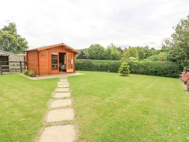 A garden with a stone path leading to a wooden shed surrounded by grass and trees at Loanview in Cornhill-On-Tweed