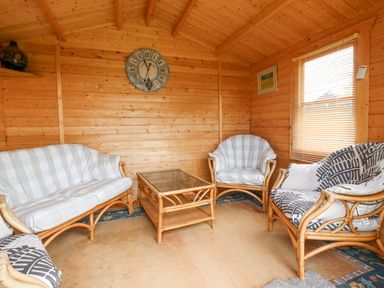 A wooden interior room with rattan furniture including a sofa two armchairs and a glass topped coffee table at Loanview in Cornhill-On-Tweed