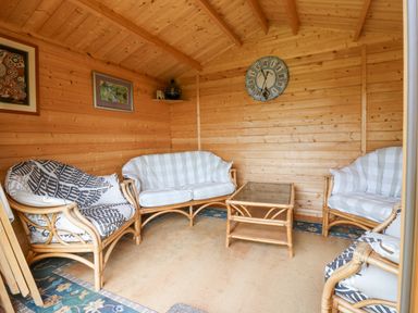 A wooden room with wicker sofas and a glass table with a clock on the wall at Loanview in Cornhill-On-Tweed