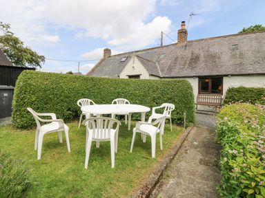 A garden with white plastic chairs and a table near a house with a hedge and a flower bed at Loanview in Cornhill-On-Tweed