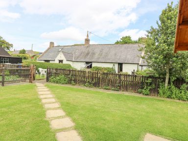 A garden with a stone path leading to a wooden gate and a white cottage behind a wooden fence at Loanview in Cornhill-On-Tweed