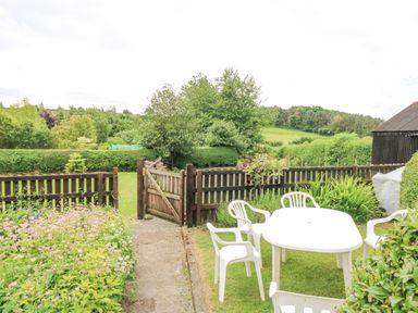 An outdoor garden area with a white plastic table and chairs on grass a wooden fence and gate with plants and trees at Loanview in Cornhill-On-Tweed