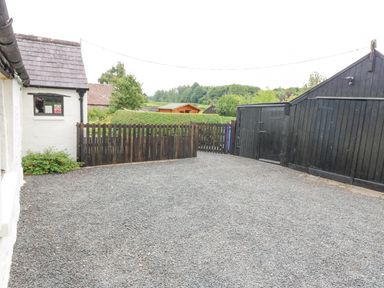 An outdoor gravel area with a wooden fence and black wooden shed at Loanview in Cornhill-On-Tweed