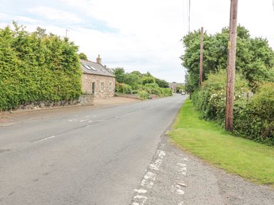 A rural road with a stone house and green hedges at Loanview in Cornhill-On-Tweed