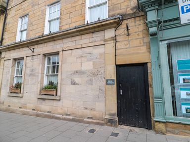 Exterior of a stone building with three windows and a black door with a sign reading Swan Cottage at White Swan Cottage in Alnwick