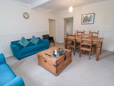 A living room with blue sofas, wooden coffee table, wooden dining table with chairs and a wall clock at White Swan Cottage in Alnwick