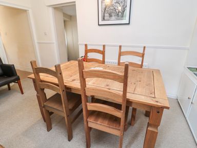 A dining room with a wooden table and four wooden chairs and a black armchair at White Swan Cottage in Alnwick