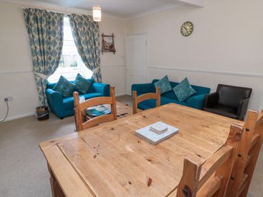 A living room with two blue sofas a black armchair a wooden dining table with chairs and patterned curtains at White Swan Cottage in Alnwick