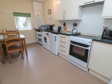 A kitchen with dining table washing machine oven and white cabinets at White Swan Cottage in Alnwick