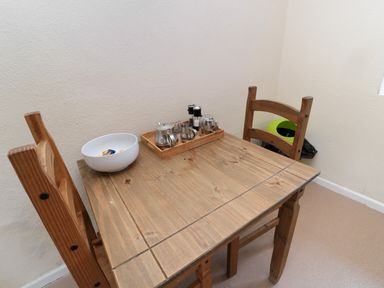 A wooden table with two wooden chairs a white bowl and a tray with condiments on the table at White Swan Cottage in Alnwick