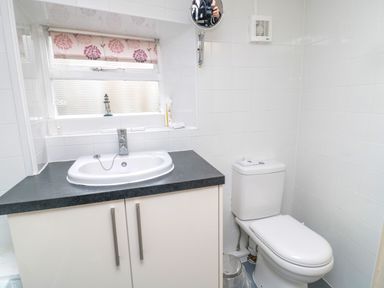 A bathroom with a sink, toilet, window with floral blind, and a small wall-mounted mirror at White Swan Cottage in Alnwick