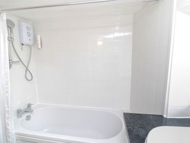 A bathroom with a white bathtub a wall-mounted shower unit and a black countertop at White Swan Cottage in Alnwick