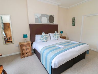 A bedroom with a double bed blue striped runner and wooden bedside tables with lamps at White Swan Cottage in Alnwick