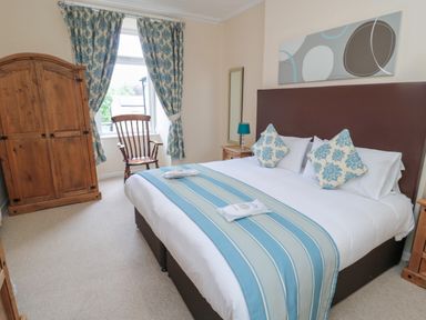 A bedroom with a double bed two patterned cushions bedside tables wooden wardrobe chair and window with curtains at White Swan Cottage in Alnwick