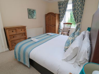 A bedroom with a double bed a wooden wardrobe chest of drawers rocking chair and window with curtains at White Swan Cottage in Alnwick