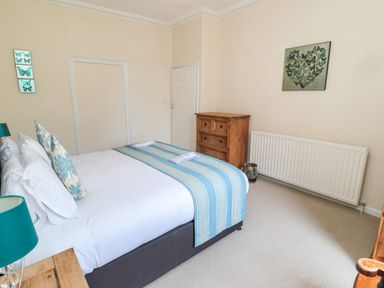 A bedroom with a double bed with blue and white linens a wooden chest of drawers and butterfly wall art at White Swan Cottage in Alnwick