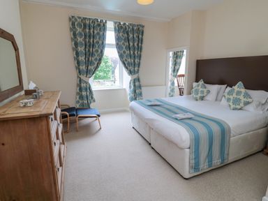 A bedroom with a double bed featuring blue striped runner and patterned pillows two chairs a wooden dresser and blue patterned curtains at White Swan Cottage in Alnwick