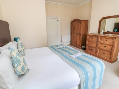 A bedroom with a bed with white linens and blue striped runner two wooden dressers and a mirror at White Swan Cottage in Alnwick