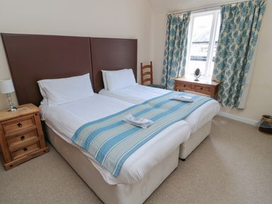 A bedroom with two single beds a wooden bedside table a lamp a window with patterned curtains and a small wooden desk at White Swan Cottage in Alnwick