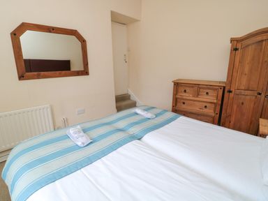 A bedroom with a bed covered with white and blue striped bedding two towels a wooden mirror a chest of drawers and a wardrobe at White Swan Cottage in Alnwick