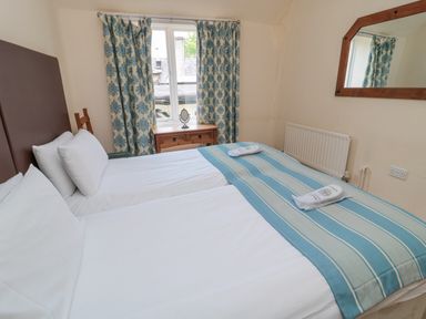 A bedroom with two single beds joined together a wooden nightstand under a window with curtains and a wall mirror at White Swan Cottage in Alnwick